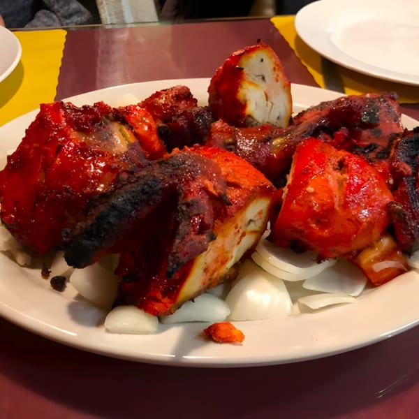 Clay Oven Restaurant's Tandoori Chicken, bright red and charred, served on a white plate with sliced onions.