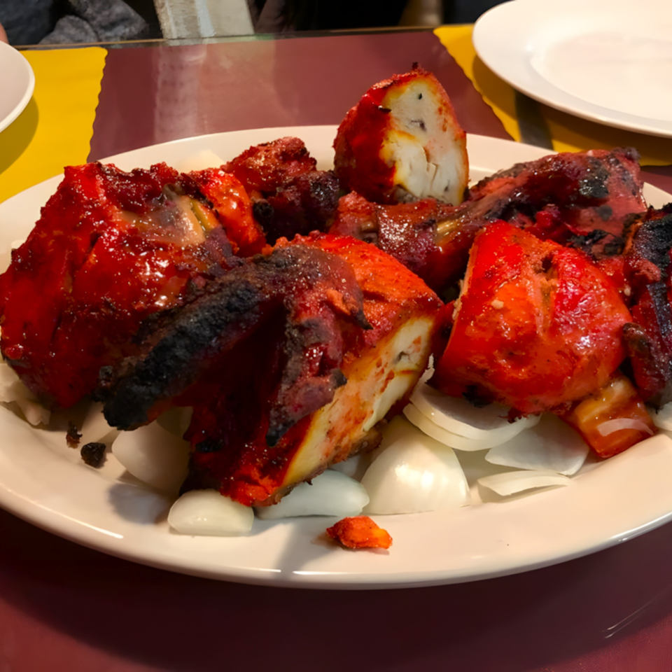 Clay Oven Restaurant's Tandoori Chicken, bright red and charred, served on a white plate with sliced onions.