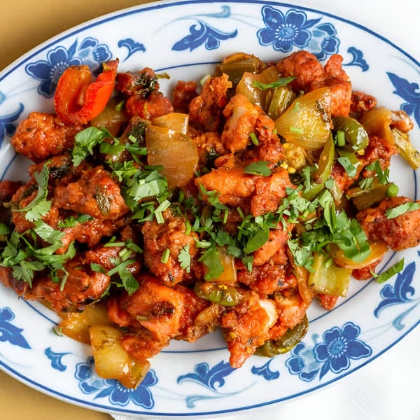 Clay Oven Restaurant's Indian chili chicken with bell peppers and cilantro on a blue and white plate.