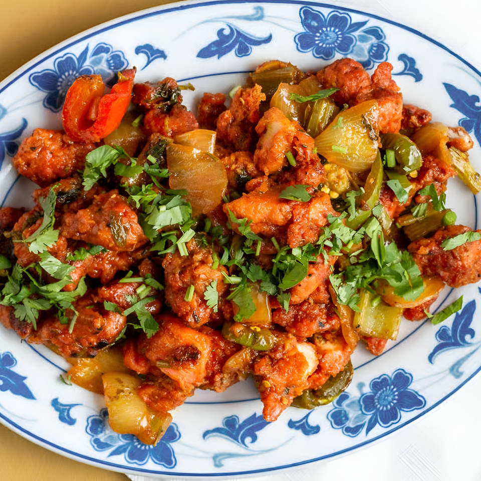 Clay Oven Restaurant's Indian chili chicken with bell peppers and cilantro on a blue and white plate.