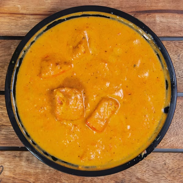 Clay Oven Restaurant's Indian butter chicken, a rich orange curry with chicken pieces in a black bowl.