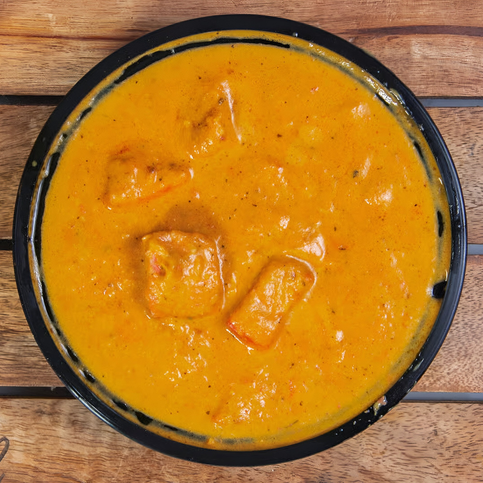 Clay Oven Restaurant's Indian butter chicken, a rich orange curry with chicken pieces in a black bowl.