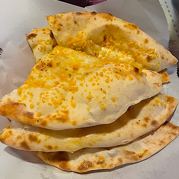 Stack of golden-brown Indian naan bread, topped with melted cheese and herbs, in a white paper-lined basket.