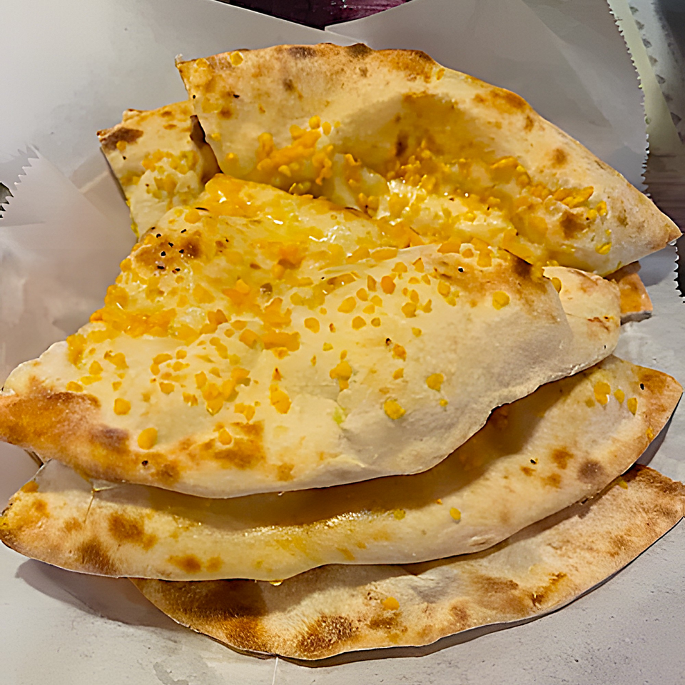 Stack of golden-brown Indian naan bread, topped with melted cheese and herbs, in a white paper-lined basket.