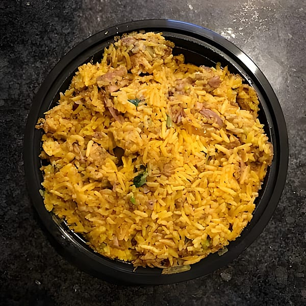 Overhead view of a black bowl filled with golden Indian biryani rice and meat.