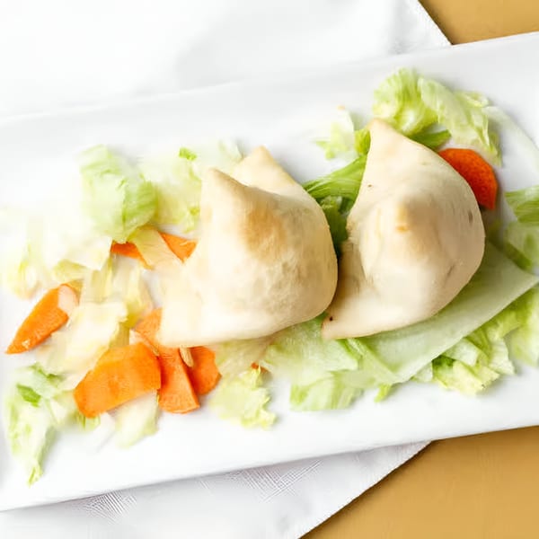 Two golden-brown Indian samosas on a white plate, garnished with fresh lettuce and carrot pieces.