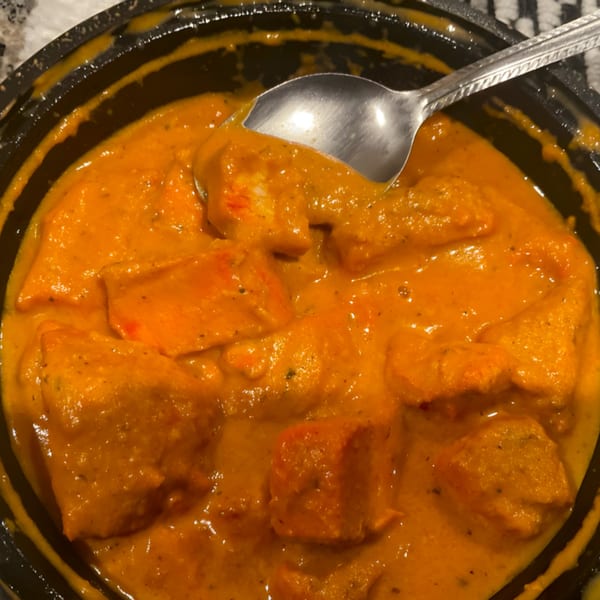 Close-up of Clay Oven Restaurant's Indian butter chicken, with a spoon in the rich orange sauce.