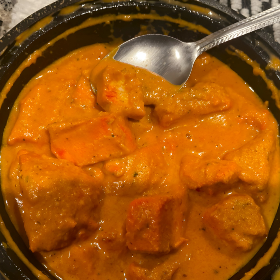 Close-up of Clay Oven Restaurant's Indian butter chicken, with a spoon in the rich orange sauce.